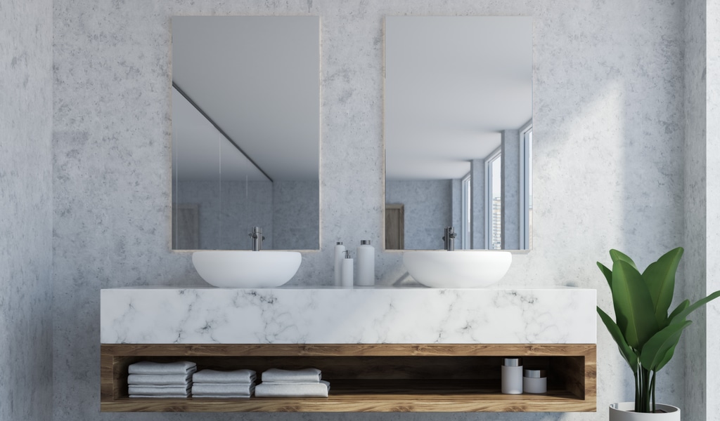 Bathroom interior with marble walls, a double sink standing on white bathroom countertops and a two vertical mirrors hanging above it.
